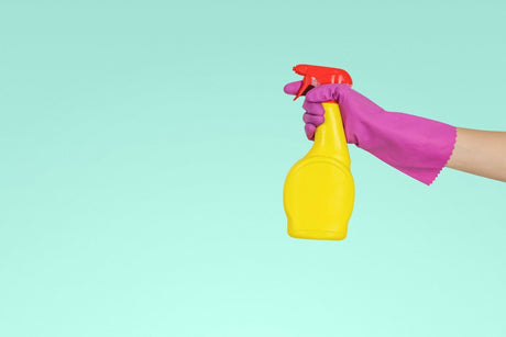 A hand holding a spray bottle wearing a purple glove showing how to clean a glass splashback