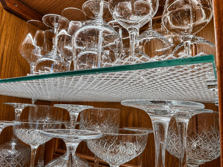 A close-up of a wooden cabinet interior with multiple clear cut-crystal wine glasses and coupe glasses arranged on glass shelves cut to size.