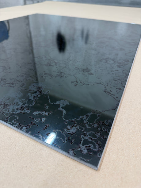 A close up of a grey antique mirror splashback on a light background showing a rusted pattern