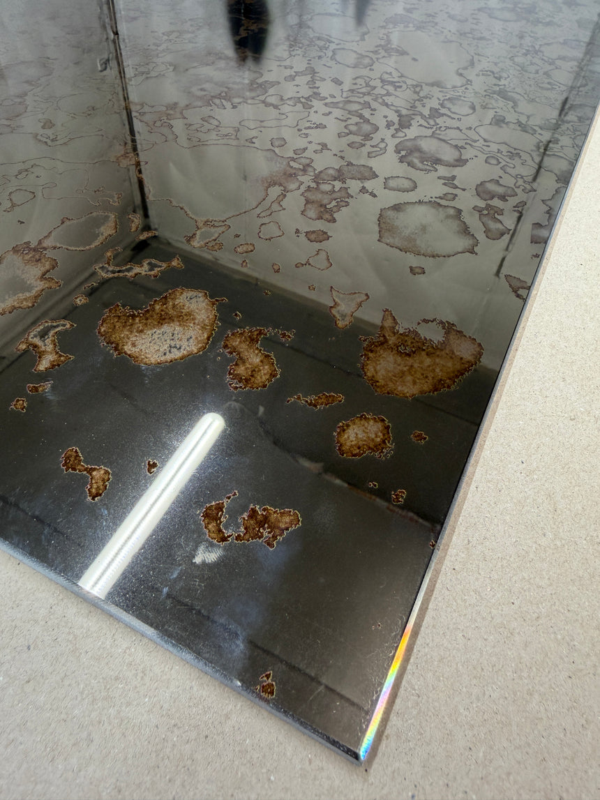 Corner of a toughened bronze antique mirror splashback showing rusting pattern
